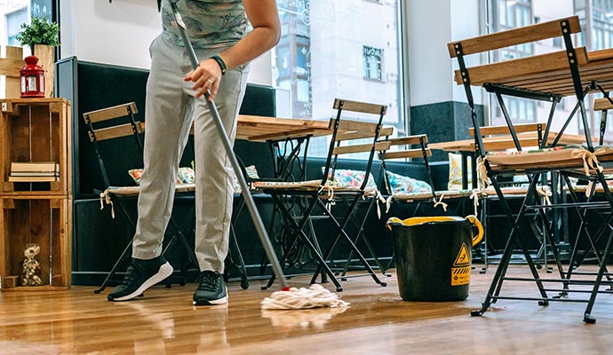 A person is cleaning a restaurant wooden floor using mob